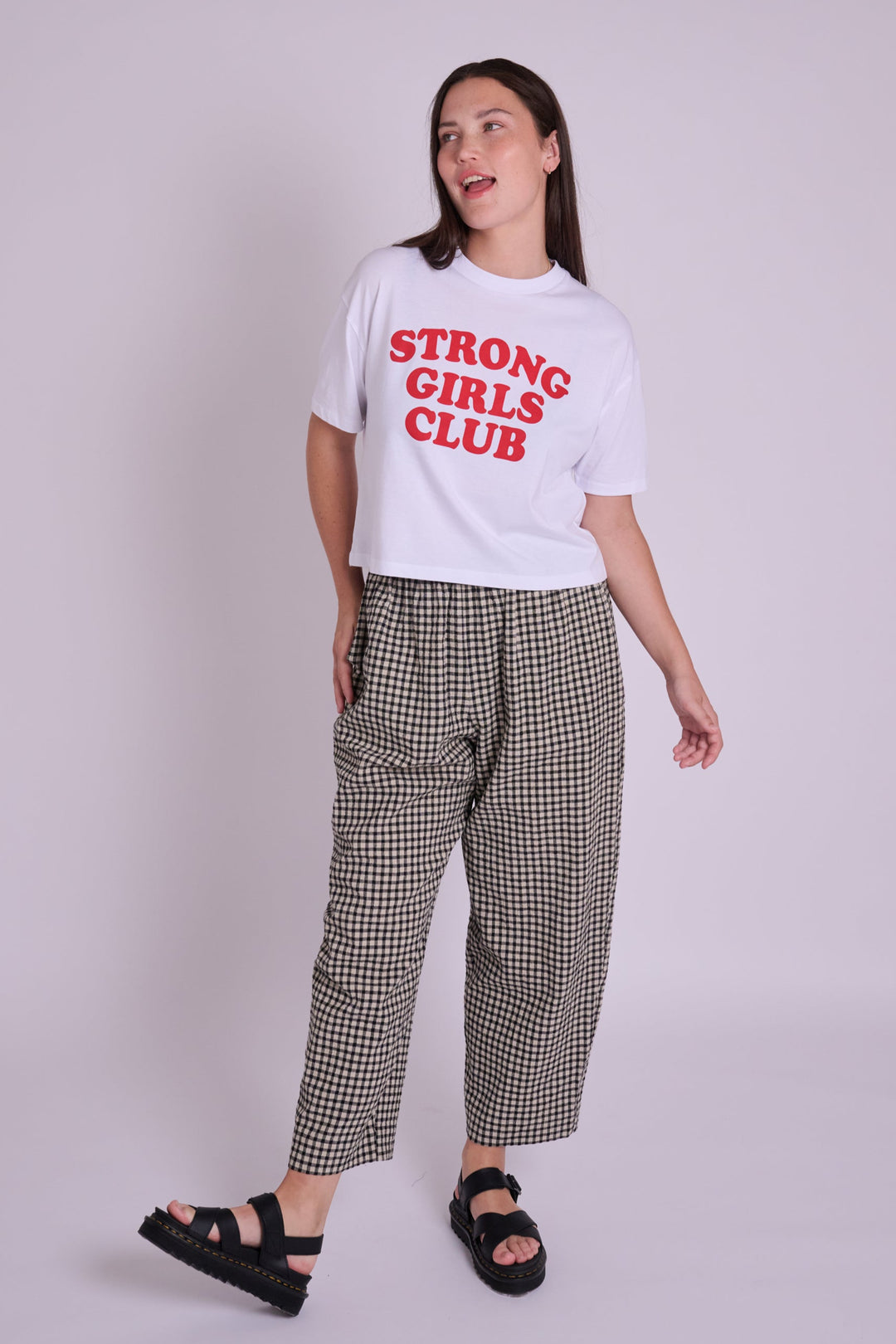Woman wearing a white t-shirt with 'STRONG GIRLS CLUB' text on a plain background