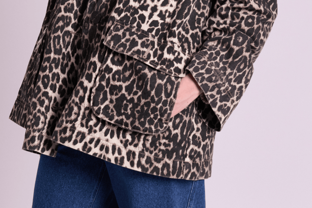 Person wearing a leopard print jacket with hands in pockets and blue jeans, against a light pink background, conveying a casual, stylish vibe.