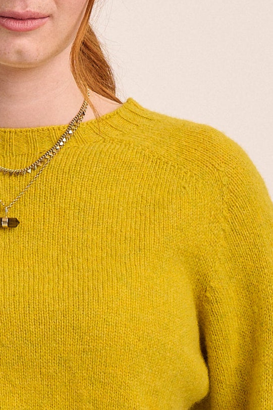 Person wearing a mustard yellow sweater and black pants on a beige background