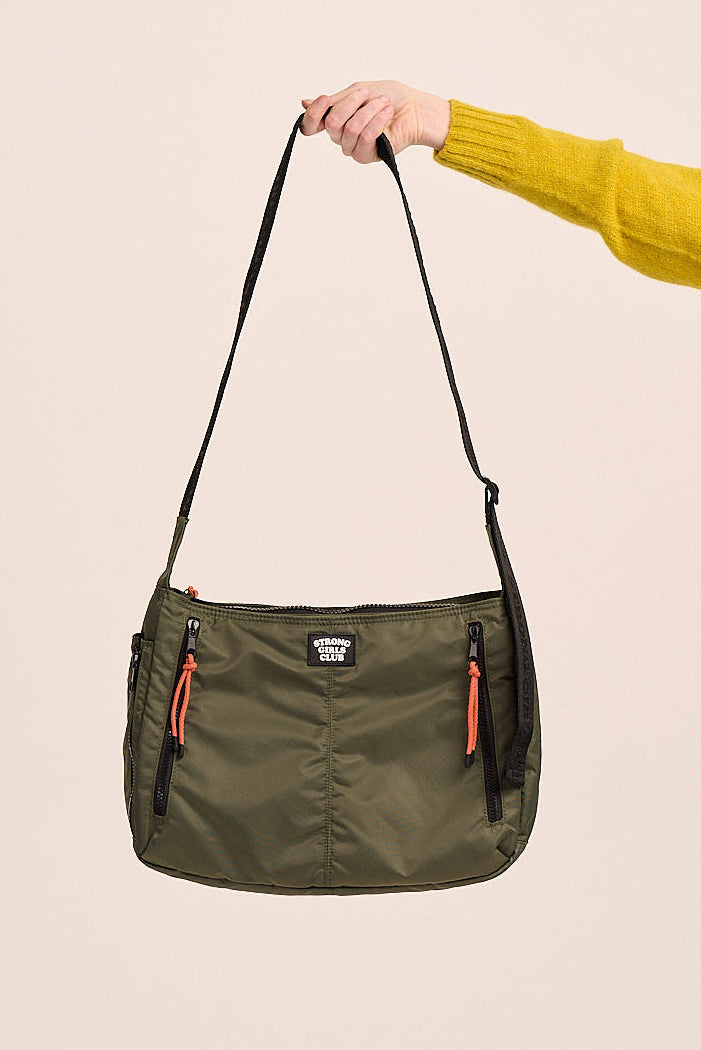 Green shoulder bag held by a hand against a beige background
