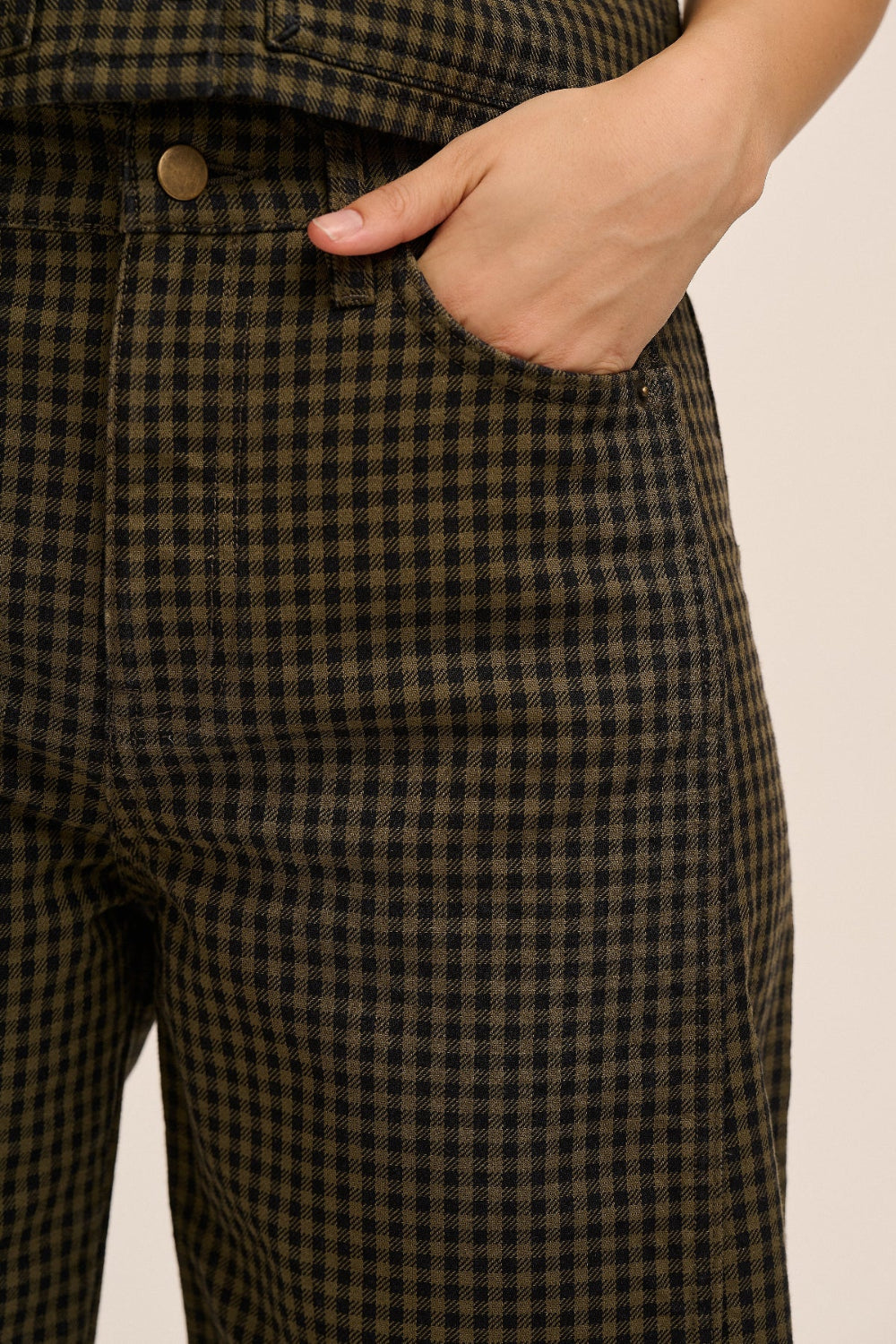 Close-up of a person wearing dark olive green and black checkered trousers, with one hand tucked into the front pocket.