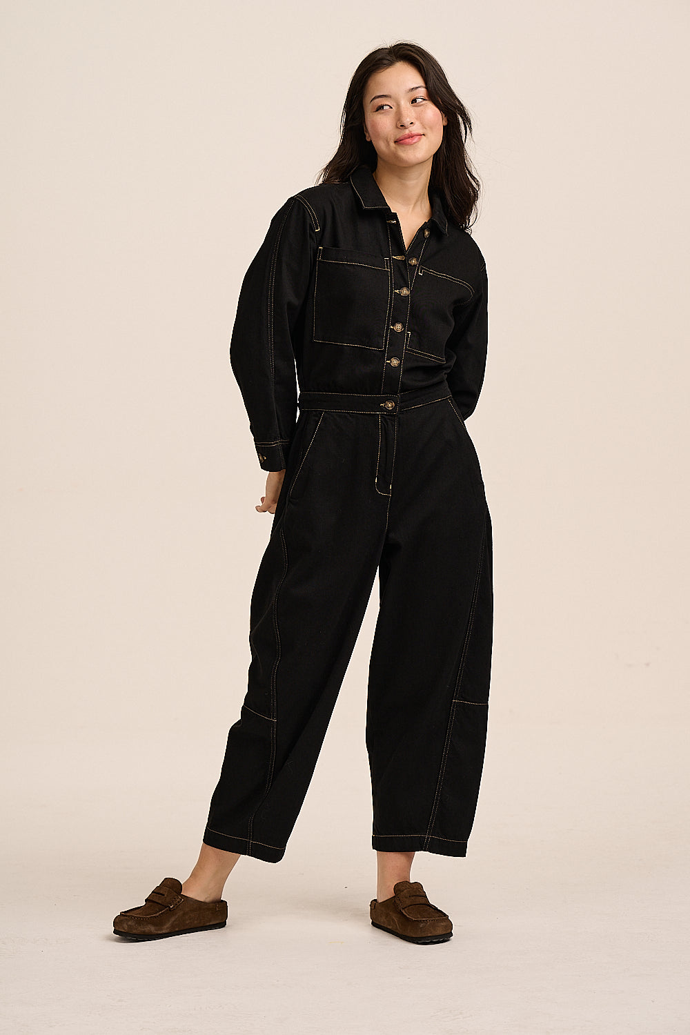 Model wearing the Gracie black denim jumpsuit, front view, with button-through front, waist tab and barrel leg