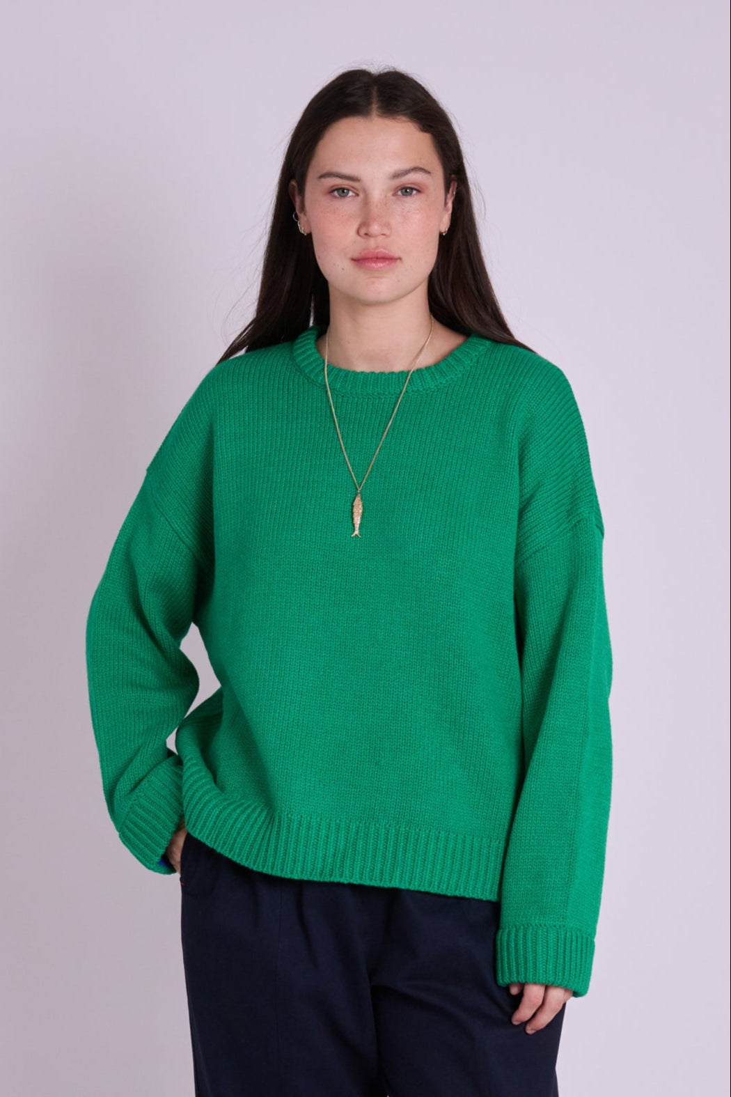 Person wearing a green sweater and black pants on a light purple background